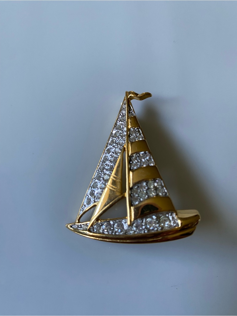 A gold-tone sailboat brooch adorned with clear stones.